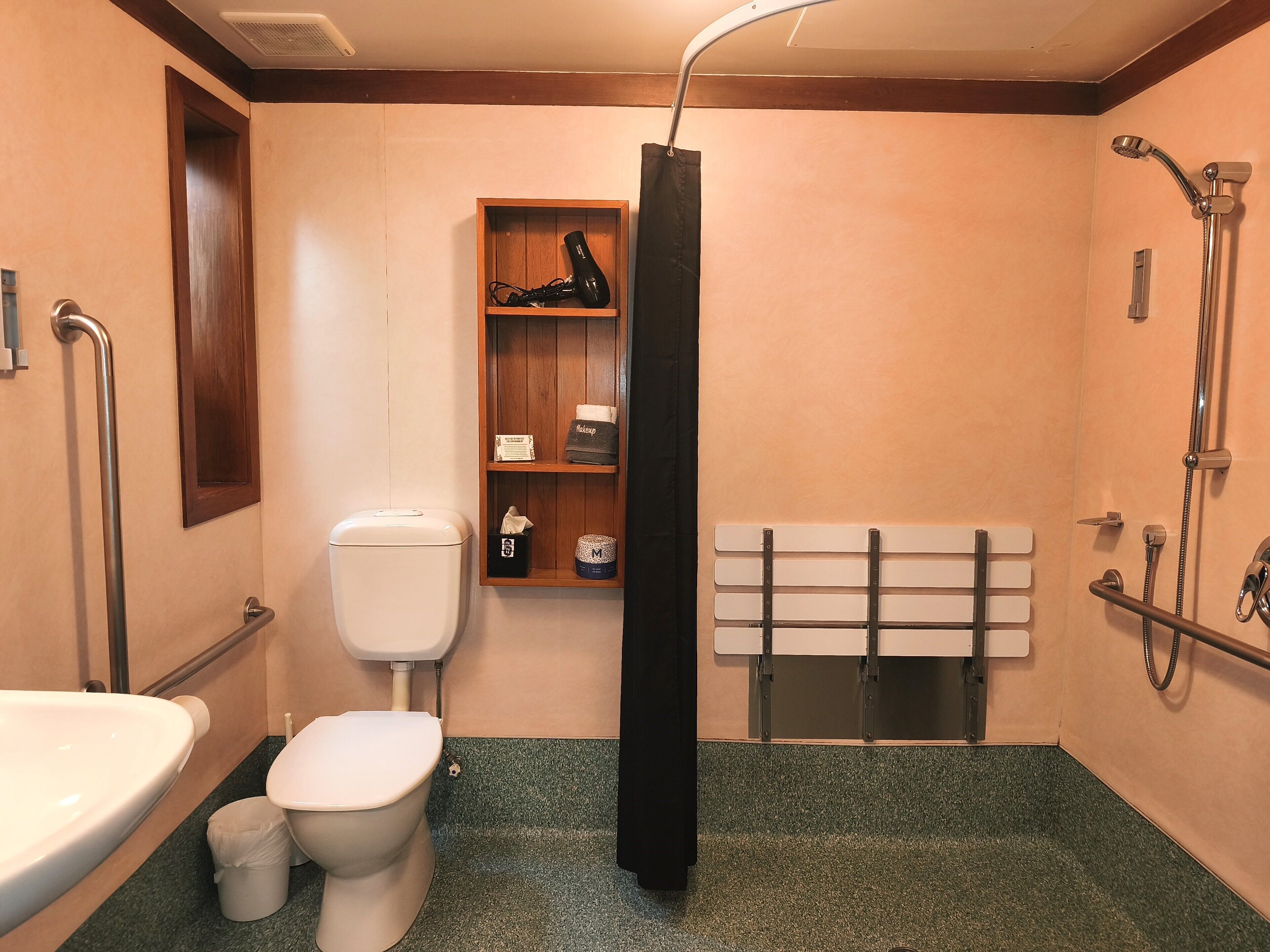 Un baño con inodoro, lavamanos, ducha y un estante con artículos de aseo.