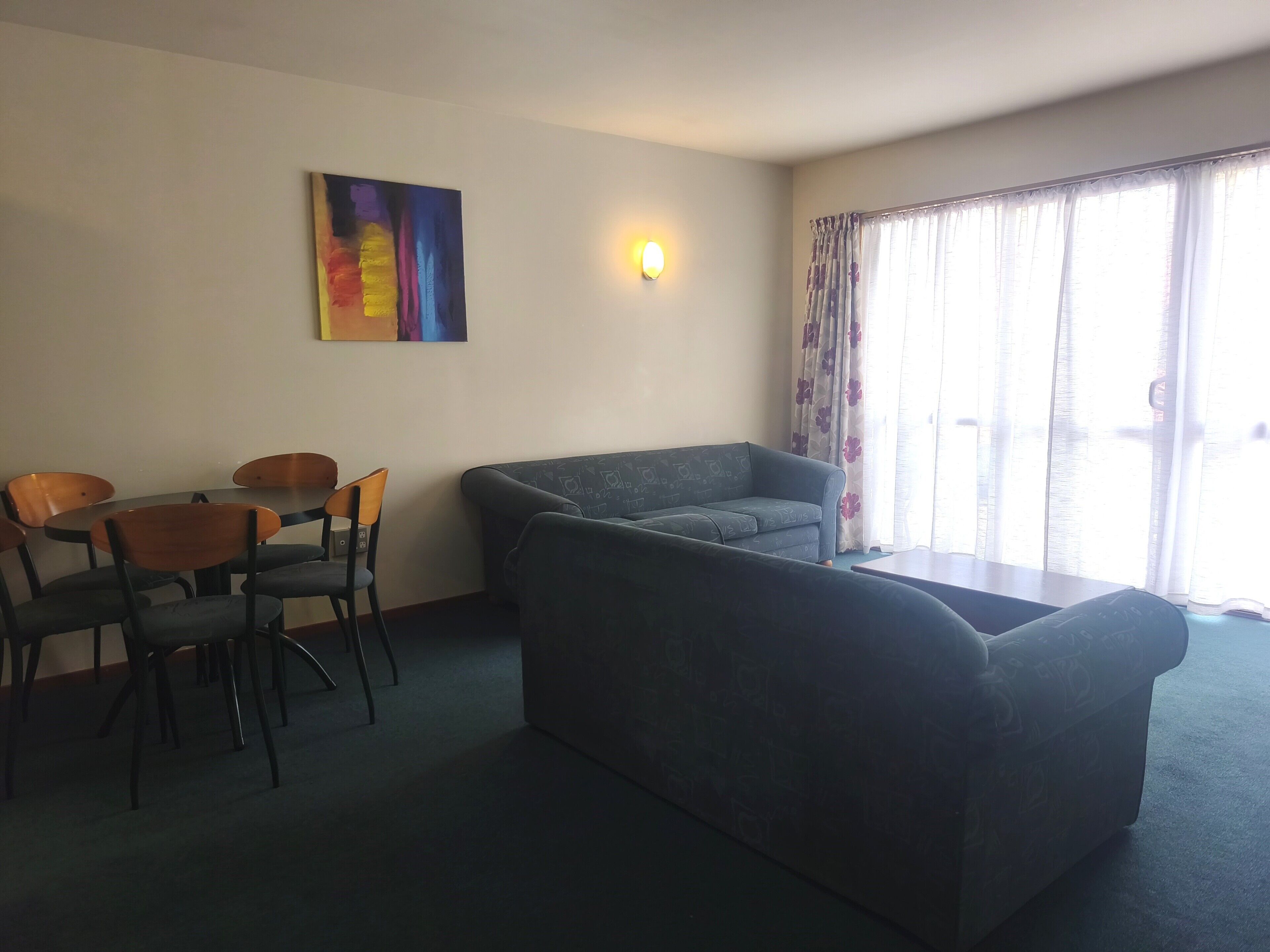 Una habitación con sofá, sillas, una mesa, un cuadro y una ventana con cortinas.
