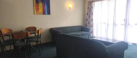 A room with a sofa, chairs, a table, a painting, and a window with curtains.