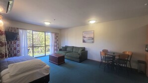 A room with a bed, a sofa, a dining table with chairs, a TV, and a window with curtains. - Aspen Lodge Motel (Hanmer Springs)