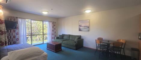 A room with a bed, a sofa, a dining table with chairs, a TV, and a window with curtains.