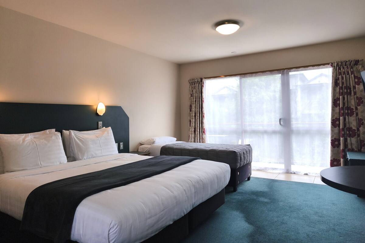 Habitación de hotel con una cama grande, otra más pequeña, un escritorio y vistas al exterior a través de un ventanal amplio.