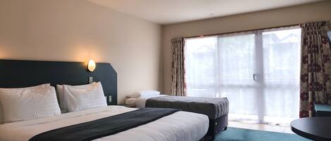 A hotel room with a large bed, a smaller bed, a desk, and a view of the outdoors through a large window.
