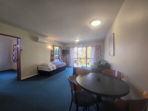 A room with a bed, a sofa, a dining table with chairs, and a television. - Aspen Lodge Motel (Hanmer Springs)