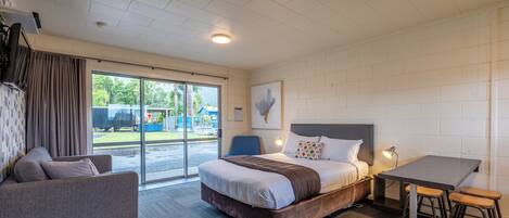 Una habitación de hotel moderna con una cama grande, un sofá, una mesa de comedor con taburetes y vistas al exterior a través de la puerta corredera de vidrio.