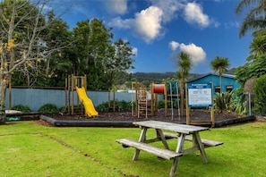 A playground with a yellow slide and climbing structures, surrounded by trees and a picnic table.