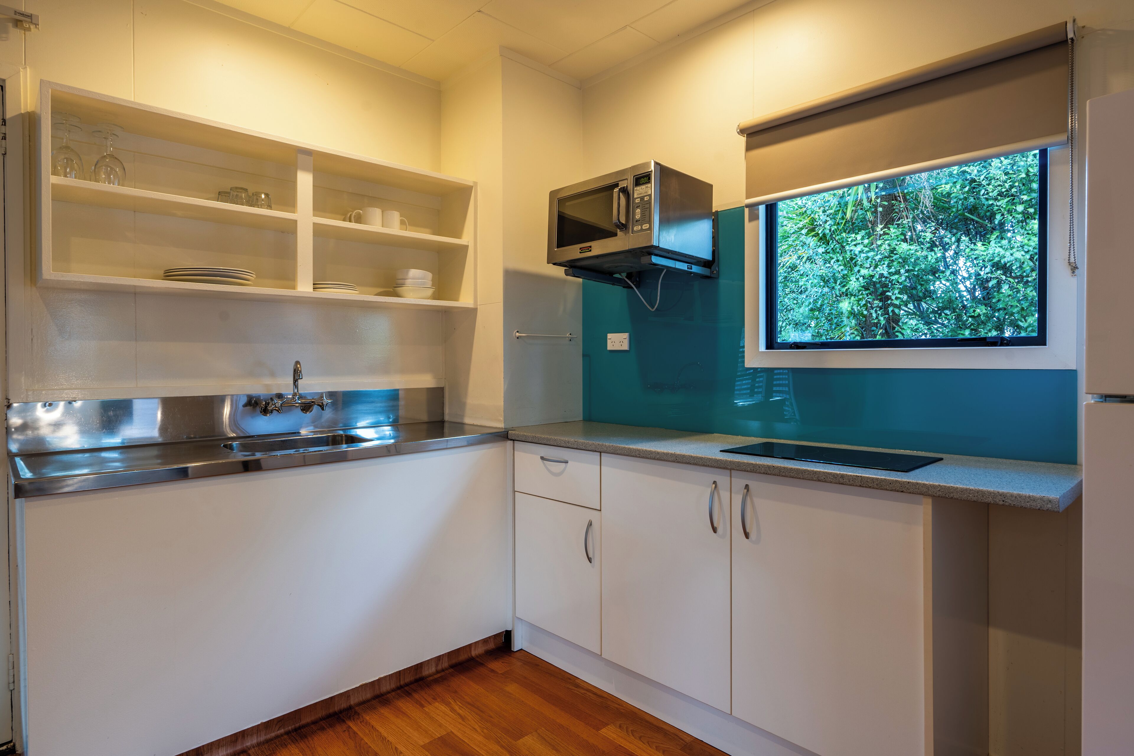Una cocina moderna con armarios blancos, un lavamanos de acero inoxidable, un microondas y una ventana con vistas al verdor.