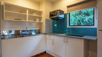 Una cocina moderna con armarios blancos, un lavamanos de acero inoxidable, un microondas y una ventana con vistas al verdor.