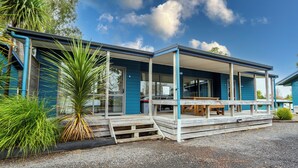 A blue building with a covered porch and a wooden bench. - Tasman Holiday Parks – Coromandel (Coromandel)