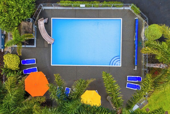 An aerial view of a swimming pool with a slide, surrounded by palm trees and lounge chairs.