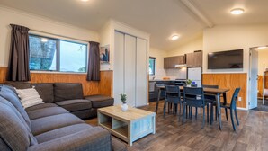 A modern living room with a sectional sofa, a wooden coffee table, and a dining area with a table and chairs. - Tasman Holiday Parks – Coromandel (Coromandel)