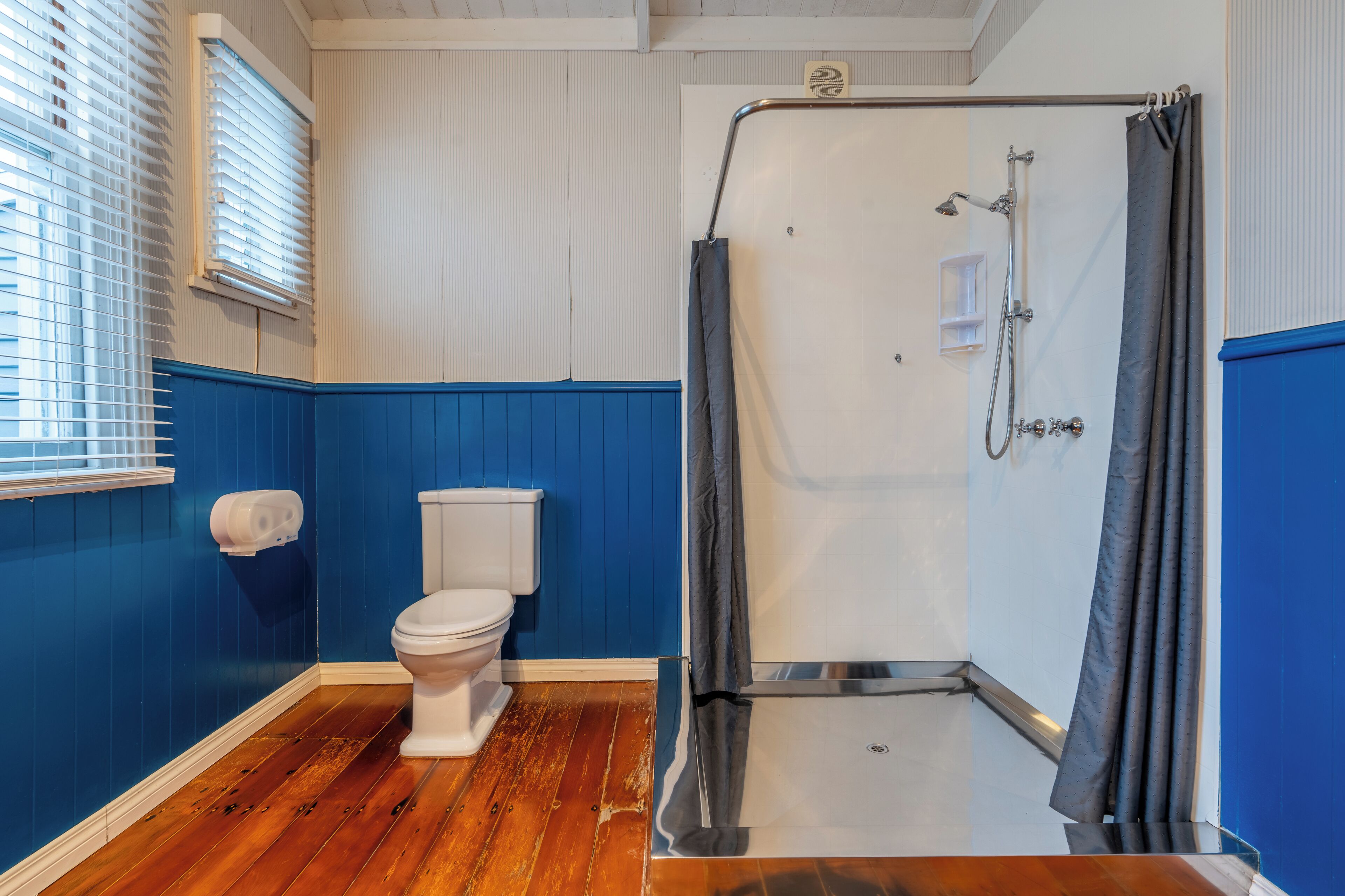 A bathroom with a white toilet, a shower with a curtain, and blue walls.