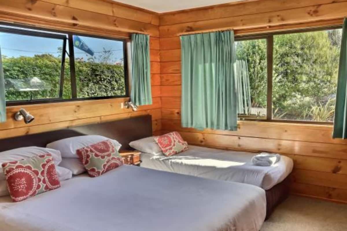 A wooden cabin room with two beds, each with a pillow and a blanket.
