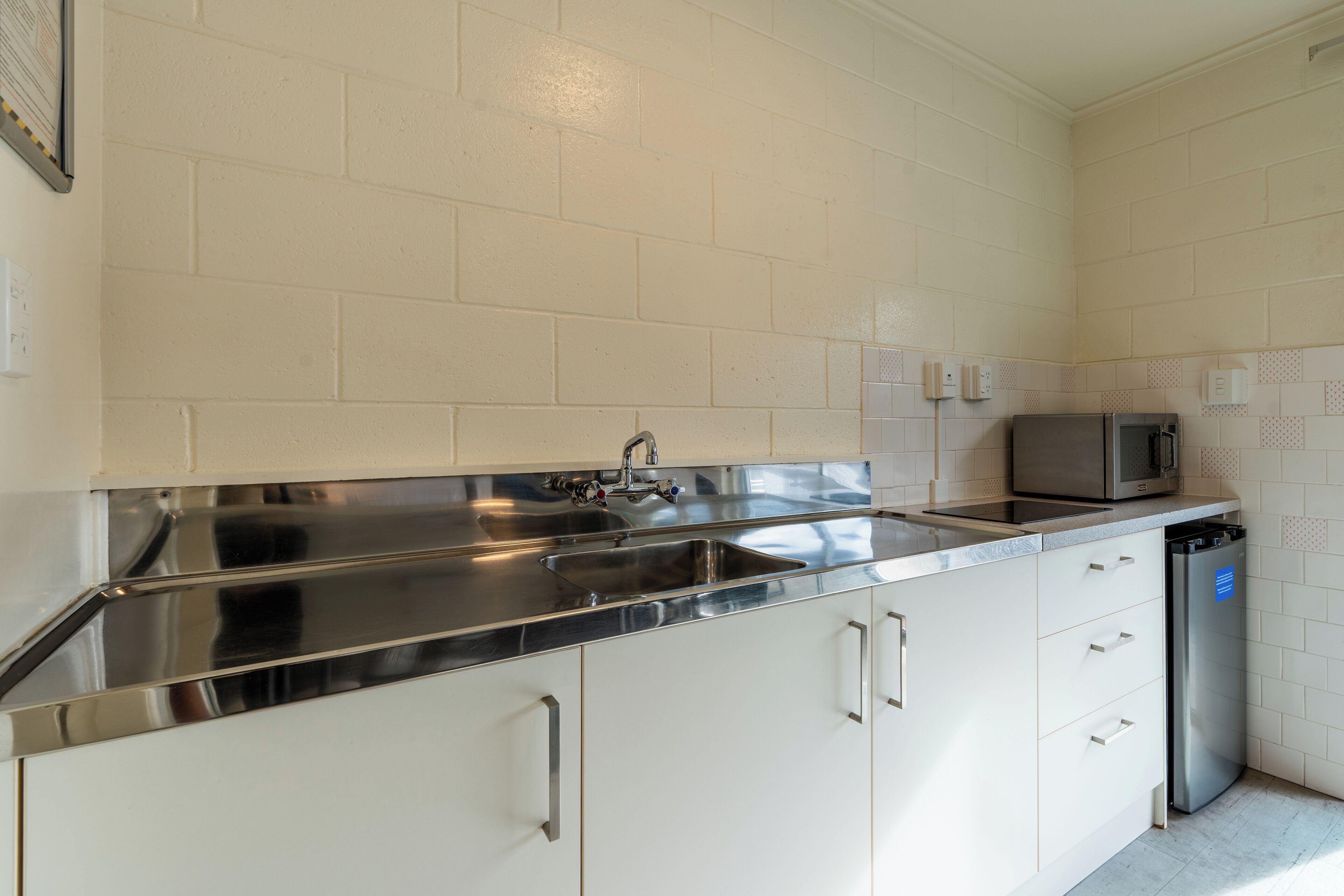 A kitchen with white cabinets, stainless steel countertops, a double sink, a microwave, and a dishwasher.