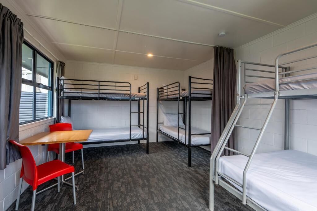 A dormitory room with bunk beds, a small table, and red chairs.
