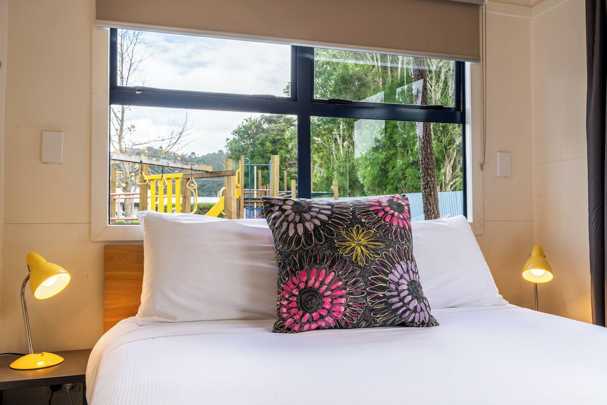 A bed with white bedding, a black and pink floral pillow, and two yellow bedside lamps.