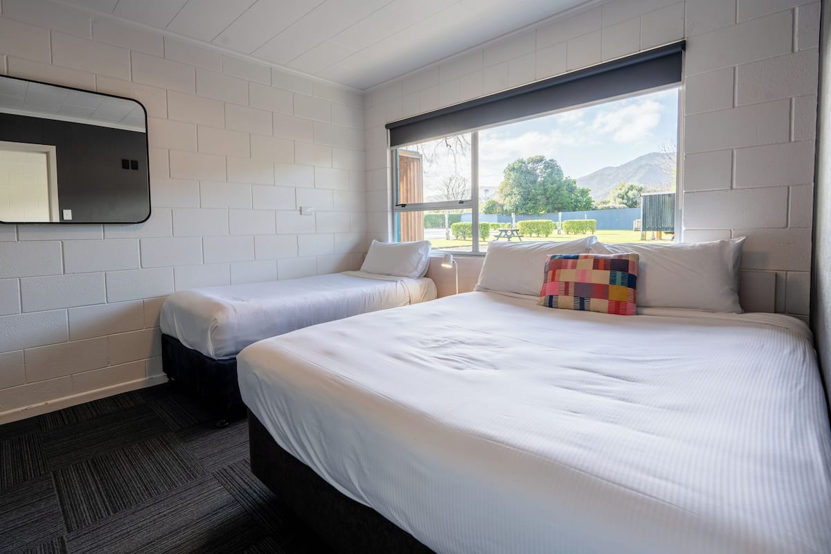 A hotel room with two beds, a large window with a view of the outdoors, and a mirror on the wall.