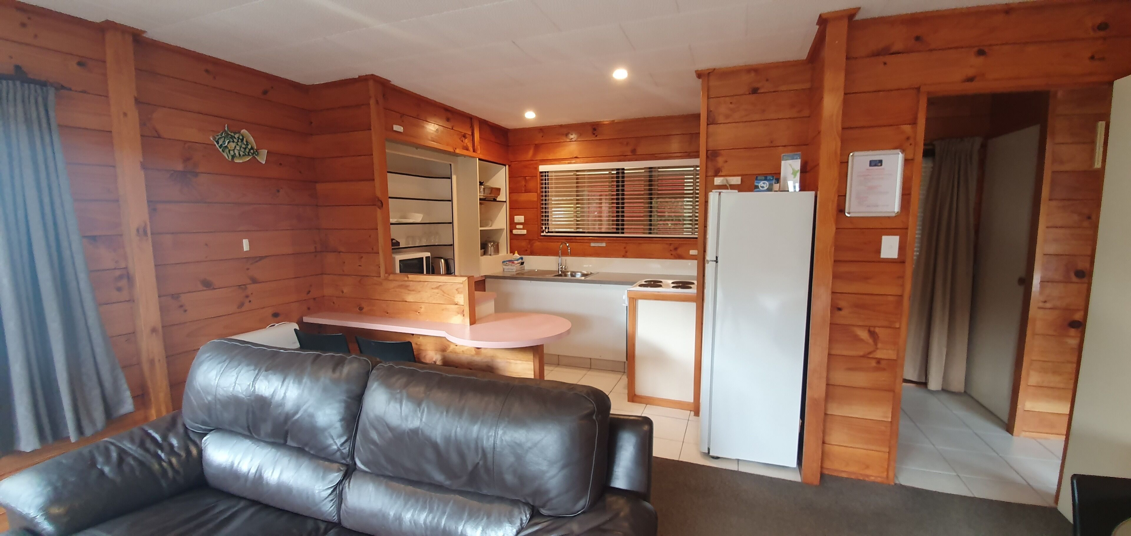 Un chalet confortable avec un canapé en cuir, des murs en bois, une kitchenette et un coin repas.