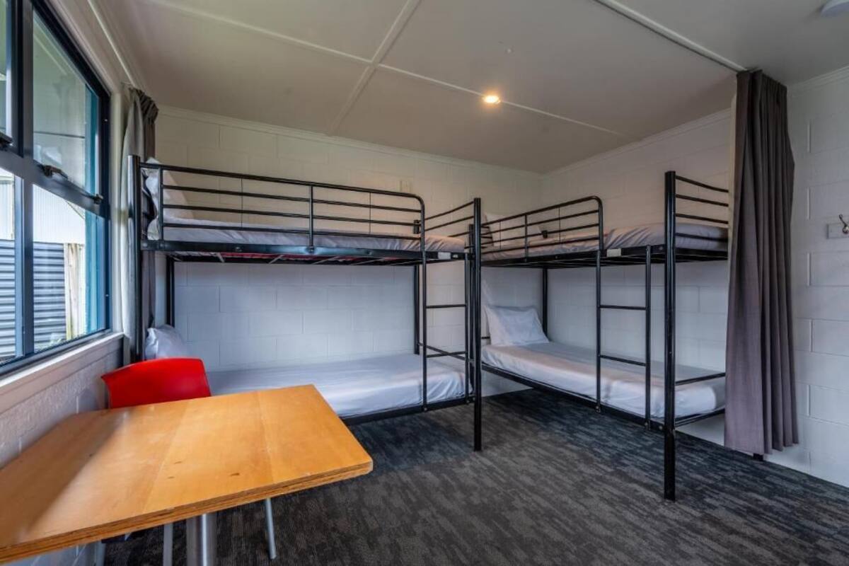 A dormitory room with bunk beds, a wooden table, and a red chair.