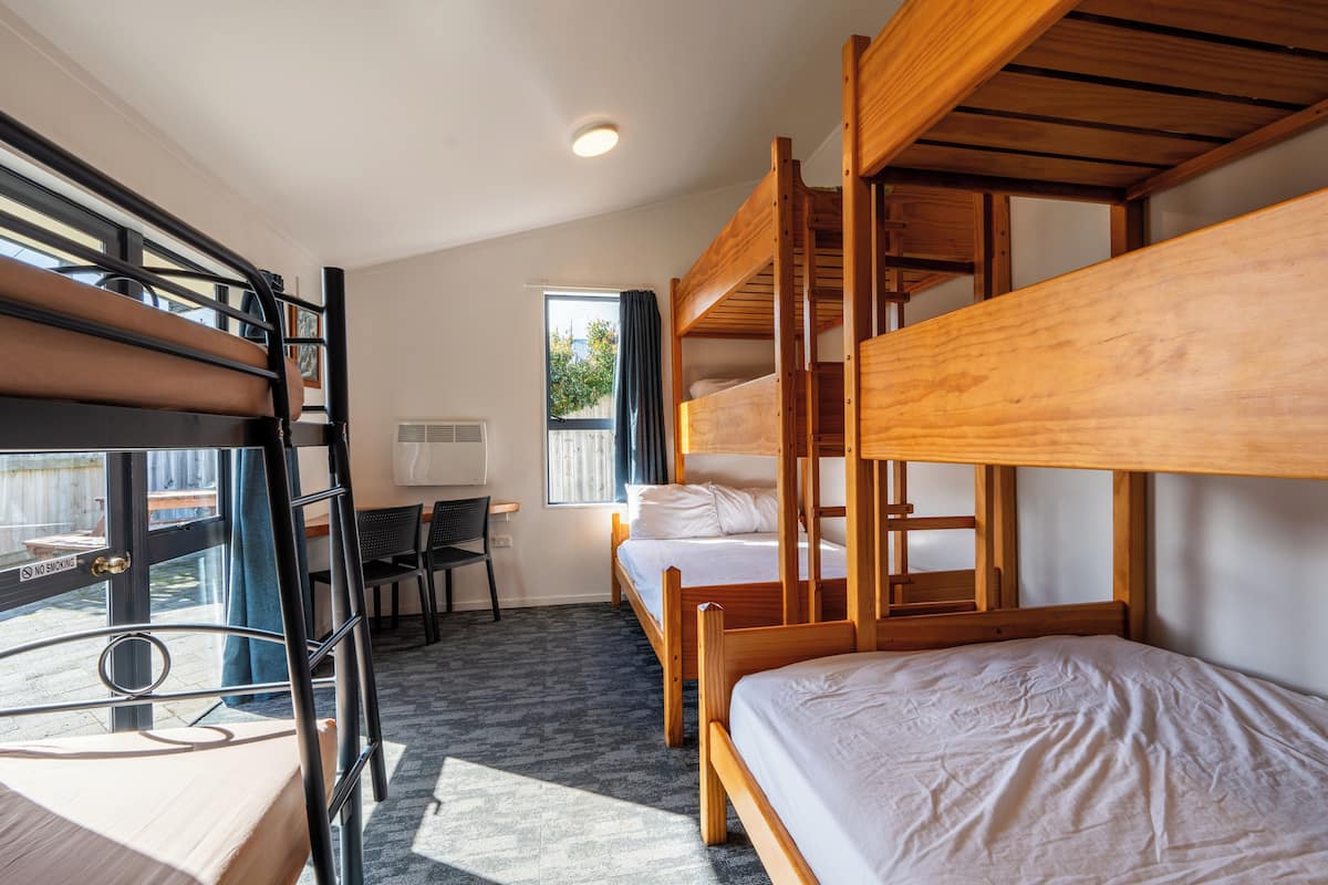 A dormitory room with bunk beds, a desk, and a window.
