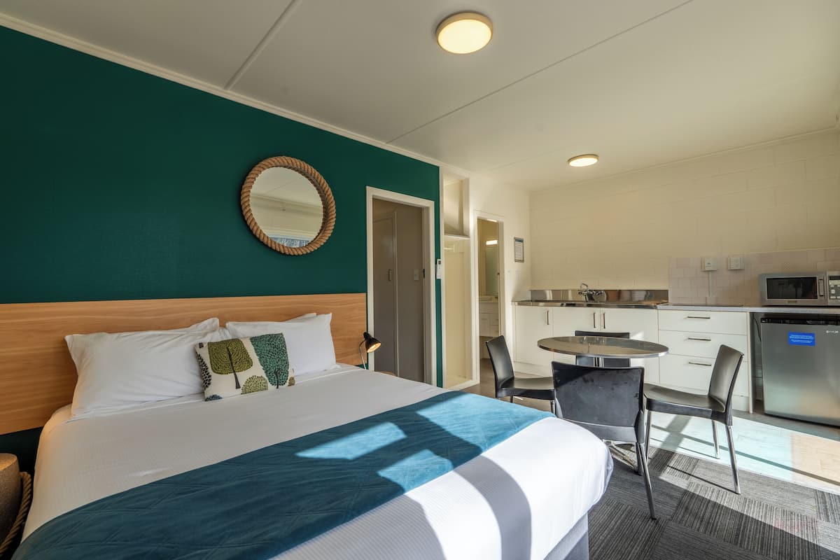 A hotel room with a bed, a round mirror, a small dining table, and a kitchenette.
