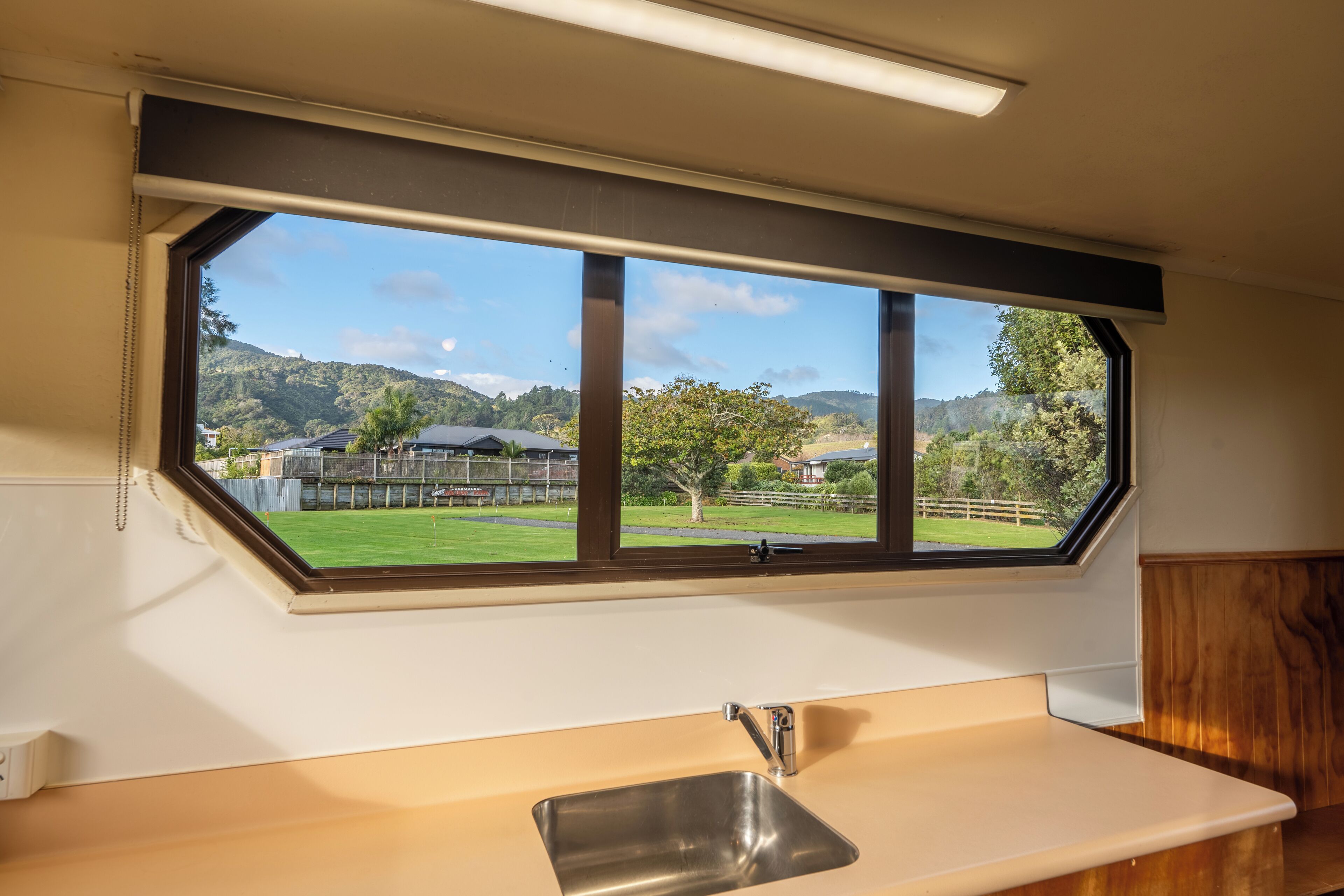 A kitchen with a window view of a green landscape and hills.