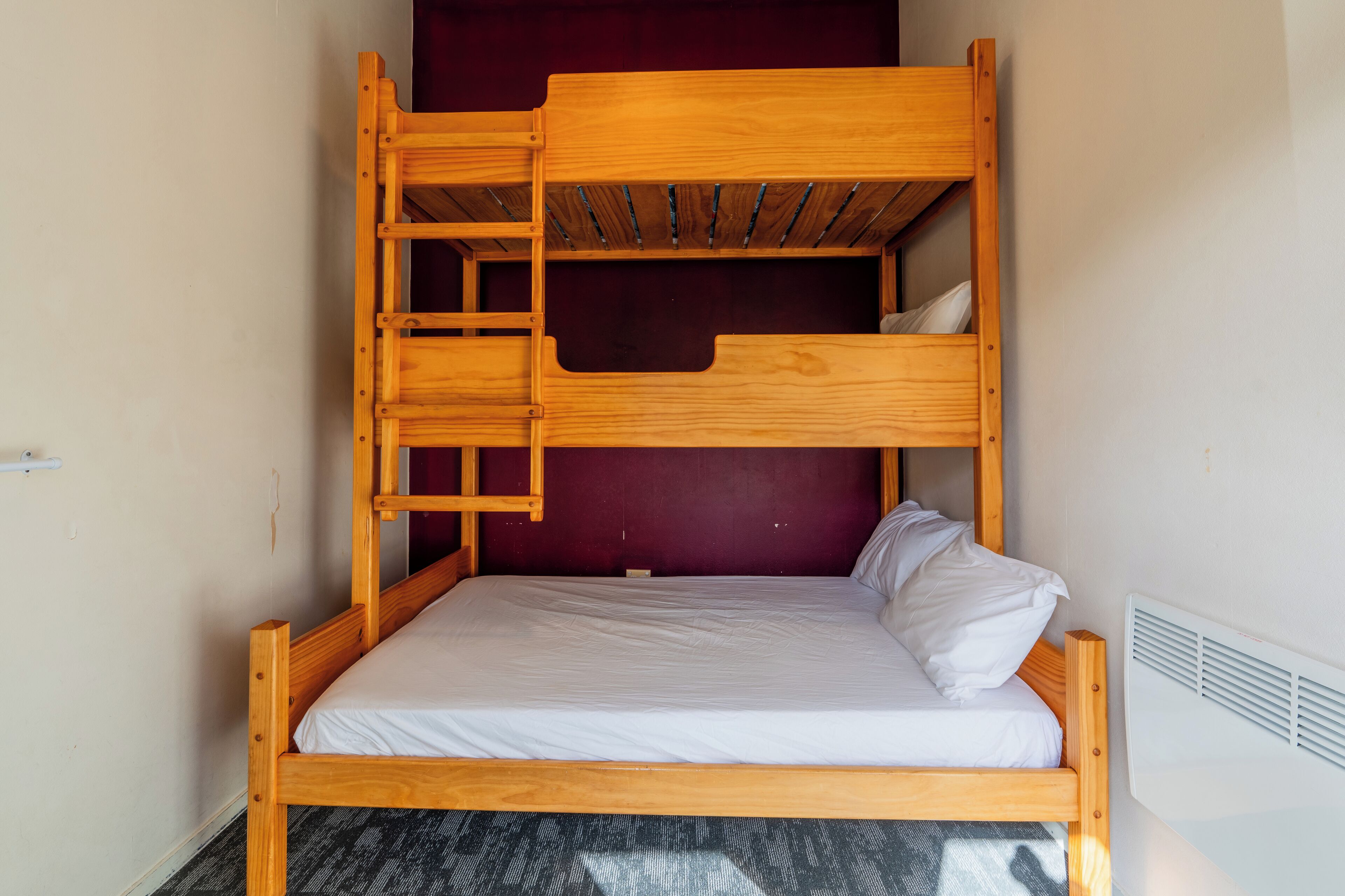 Een stapelbed met houten frame, witte beddengoed en een rode muur erachter.