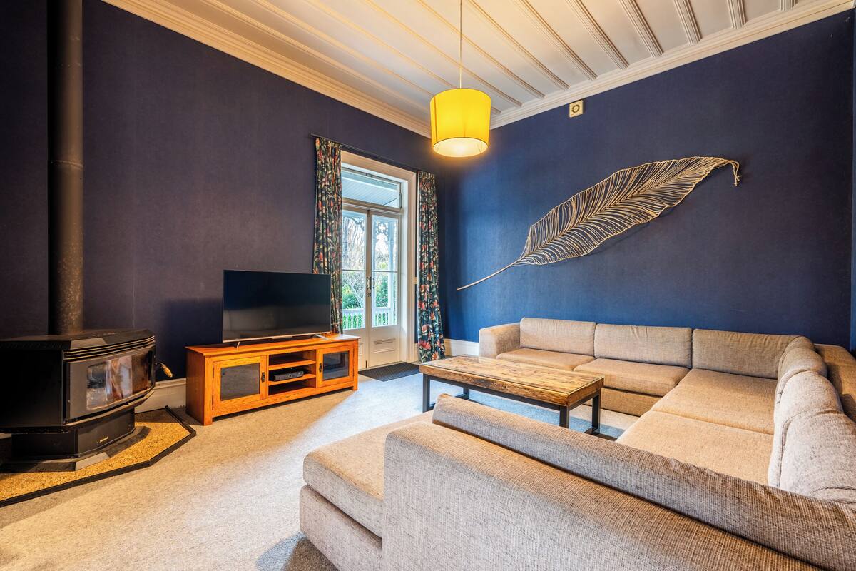 A living room with a sofa, a coffee table, a TV on a wooden stand, a fireplace, and a decorative feather on the wall.