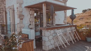A rustic stone building with a bar area featuring wooden chairs and a large vase. - Chigdem Hotel - Special Class (Cesme)