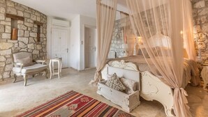 A bedroom with a stone wall, a bed with a canopy, a chair, and a small table. - Chigdem Hotel - Special Class (Cesme)
