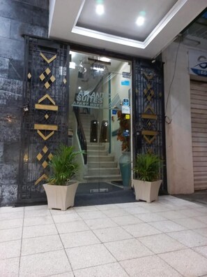 Una entrada de hotel con diseño moderno, que incluye una puerta de cristal, una escalera que da a la entrada y plantas en macetas.