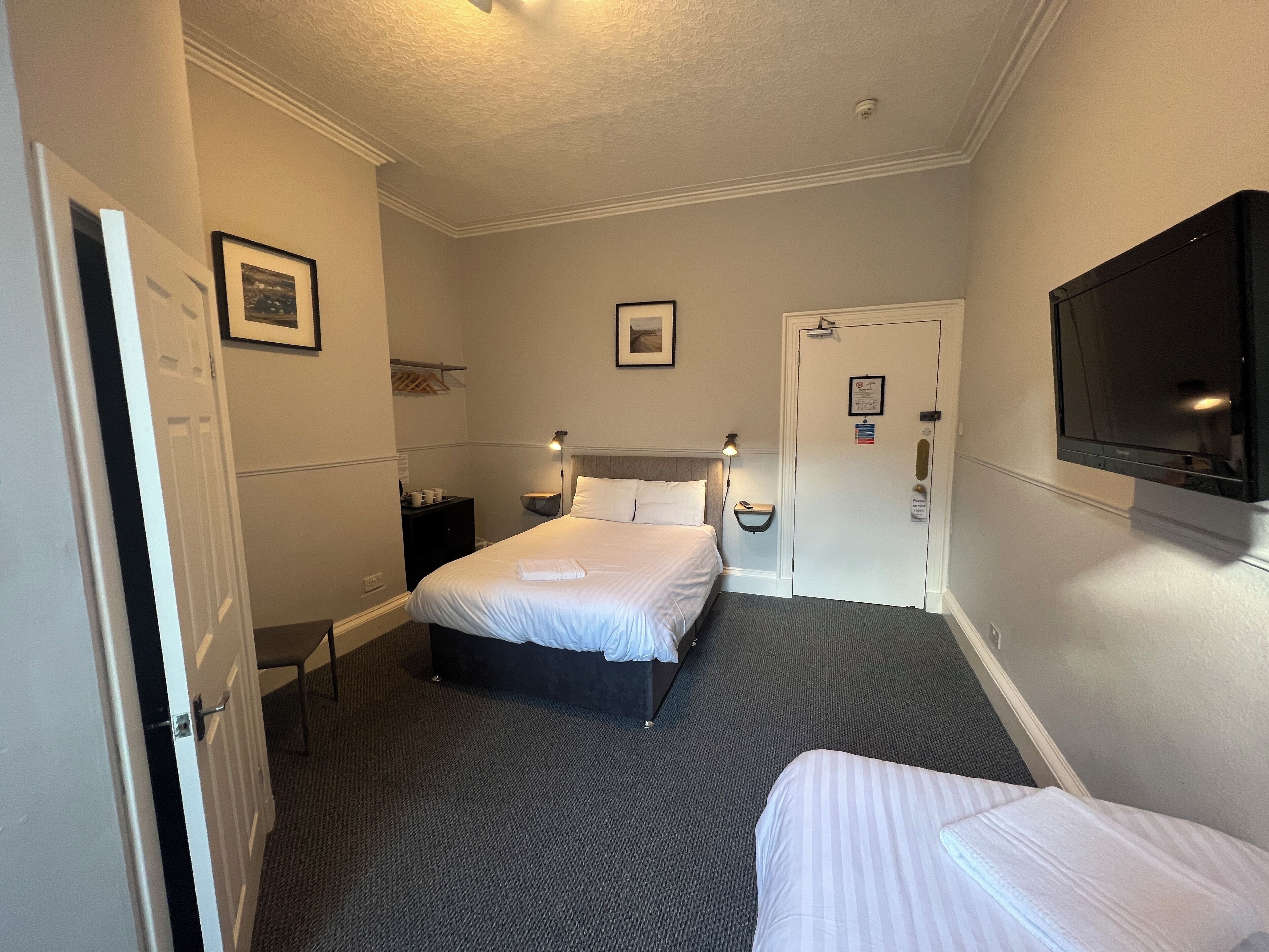 A hotel room with a bed, a bedside table, a lamp, a TV, and a door.