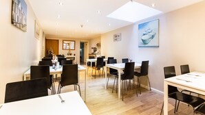 A spacious dining area with multiple tables and chairs, a kitchen in the background, and artwork on the walls. - Lost Guest House - Aberdeen (Aberdeen)