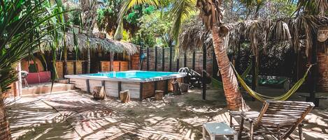 A pool area with a hammock, lounge chairs, and a thatched-roof structure.