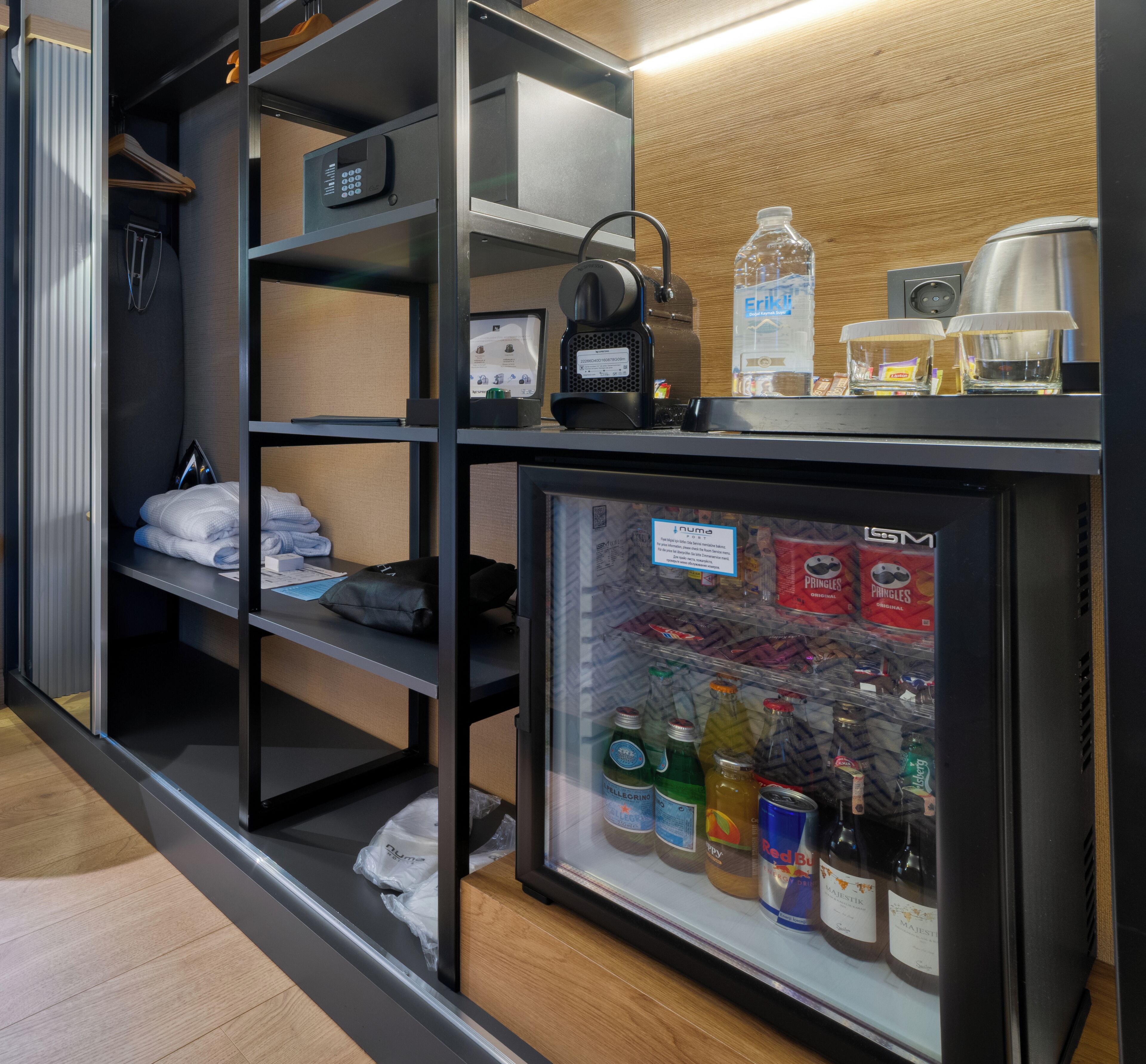 Ett hotellrum med en minibar, hyllor med hygienartiklar och ett kylskåp fyllt med drycker.