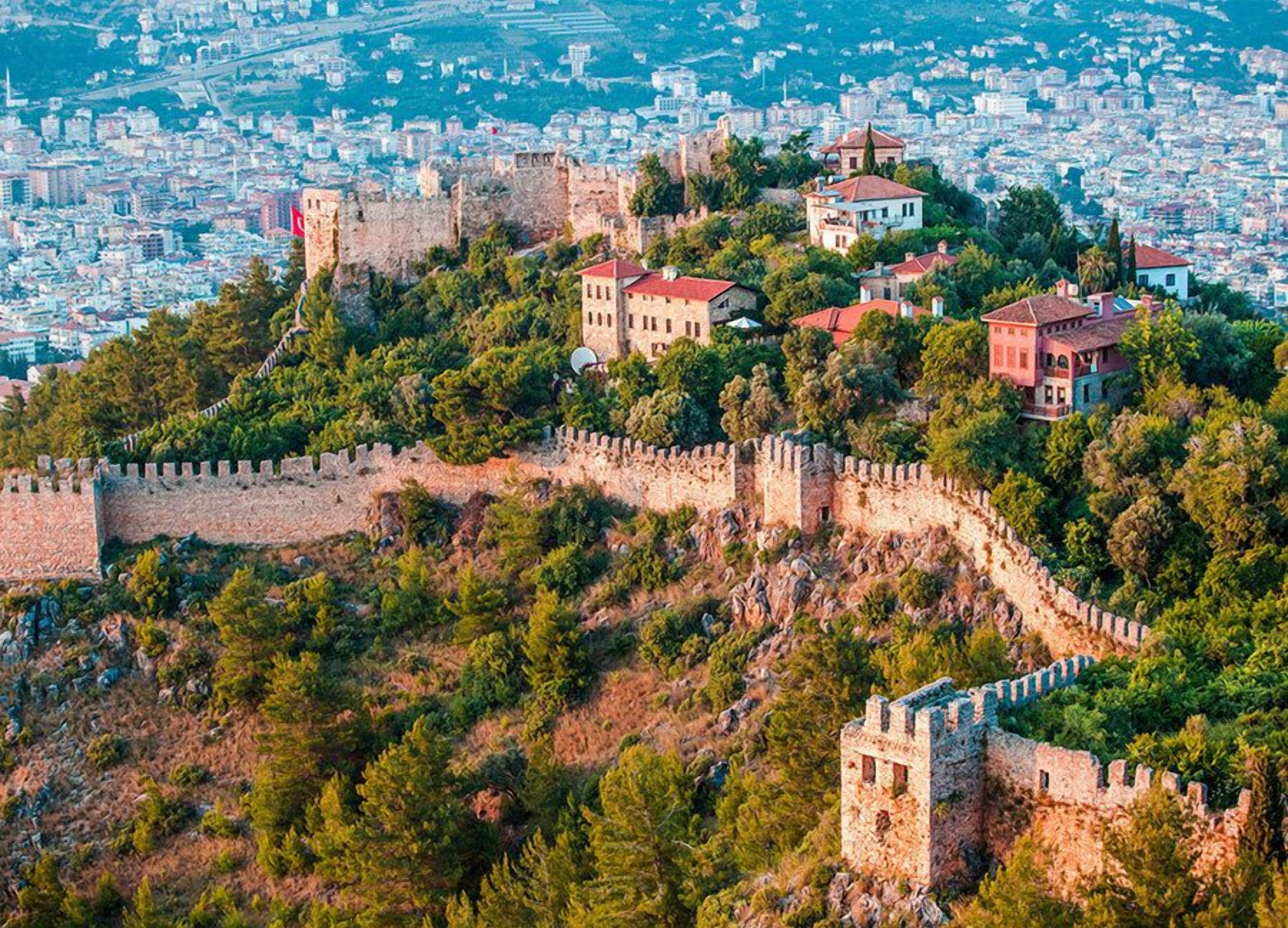 Un paisaje urbano histórico con un castillo destacado en una colina, rodeado de exuberante vegetación y edificios residenciales.
