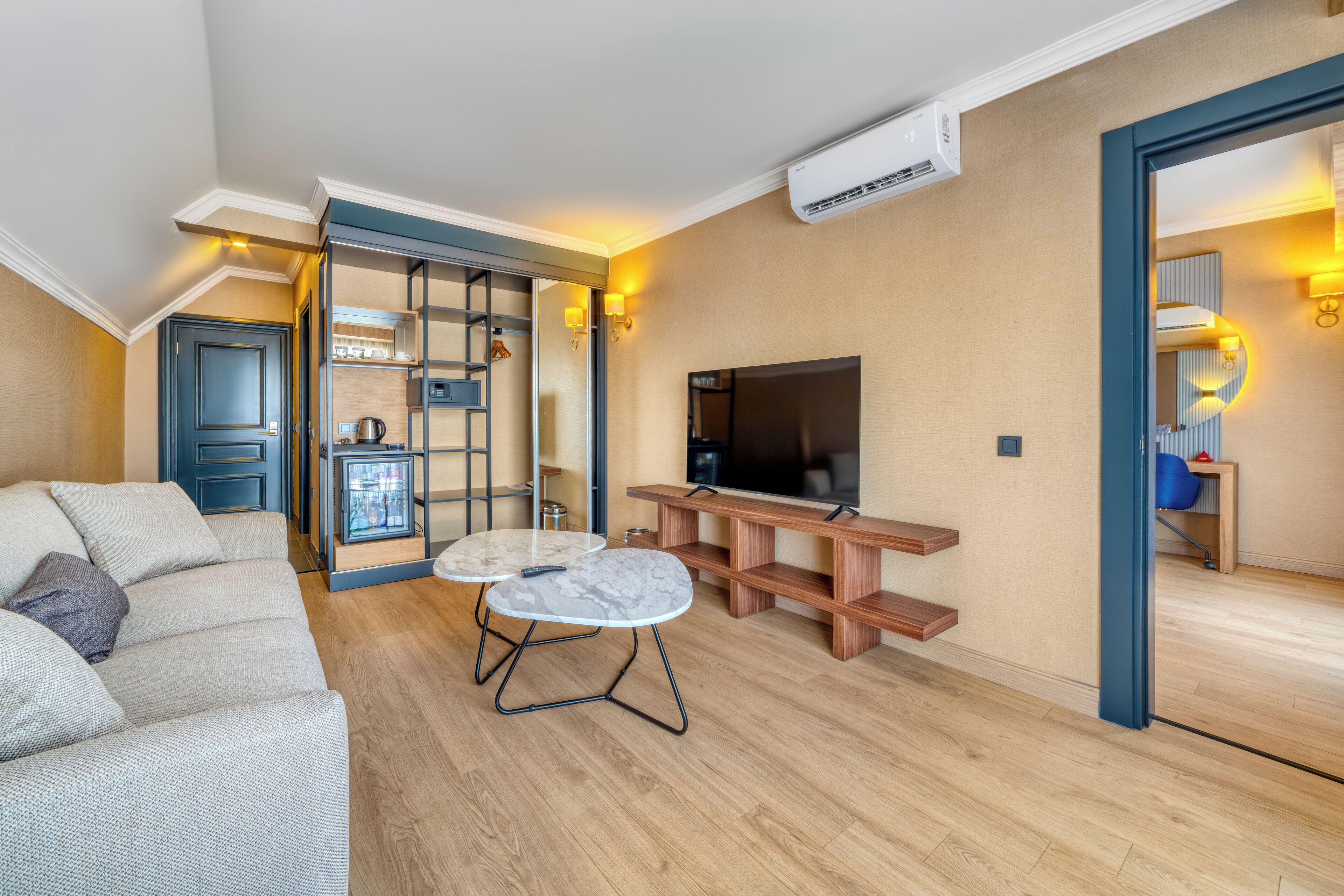 Una sala de estar moderna con un sofá, una mesa de centro, un televisor y una cocina visible a través de una división de vidrio.
