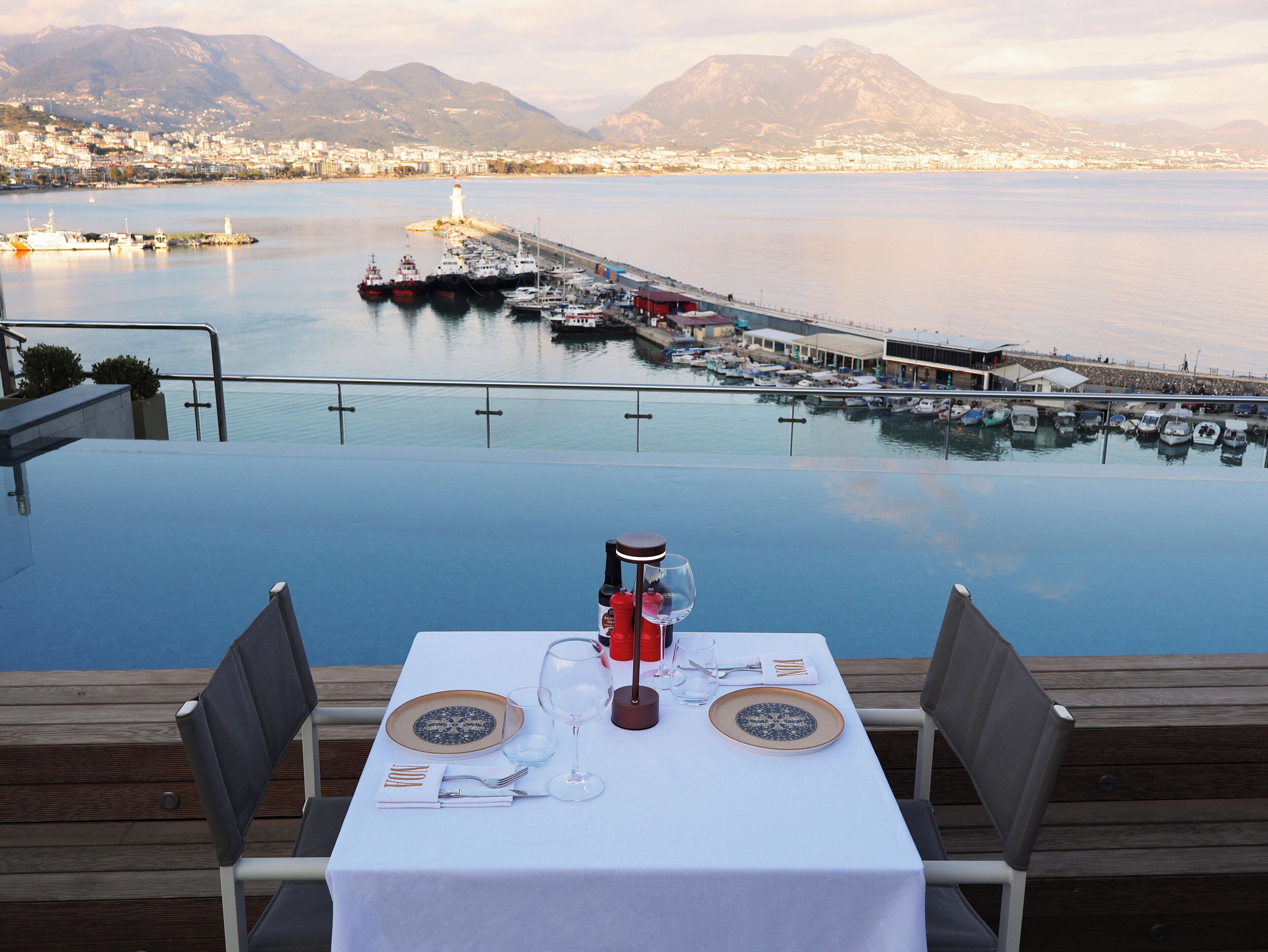 A table set for two with a view of a marina and mountains in the background.