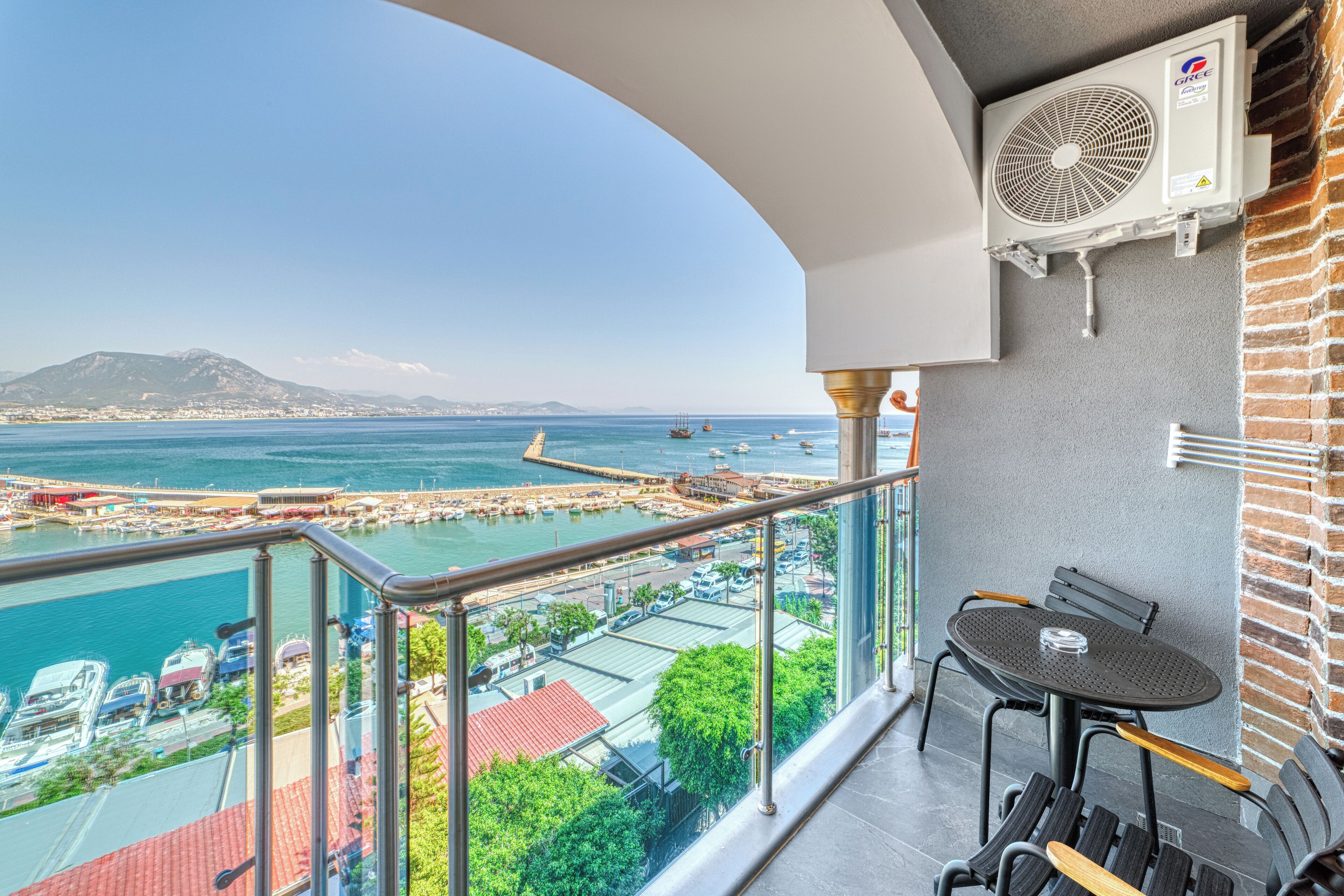A balcony with a view of a marina, a table, chairs, and an air conditioning unit.