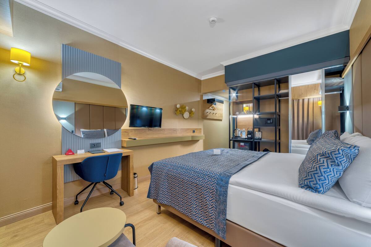 A modern hotel room with a bed, desk, chair, and a TV.