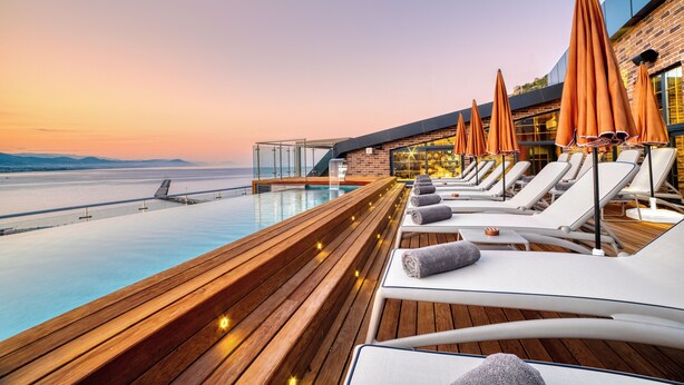 A sunlit outdoor lounge area with wooden decking, white lounge chairs, and orange umbrellas. - Numa Port Hotel (Alanya)