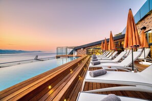 A sunlit outdoor lounge area with wooden decking, white lounge chairs, and orange umbrellas. - Numa Port Hotel (Alanya)
