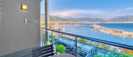 A balcony with a view of a coastal city, a table, and a chair.