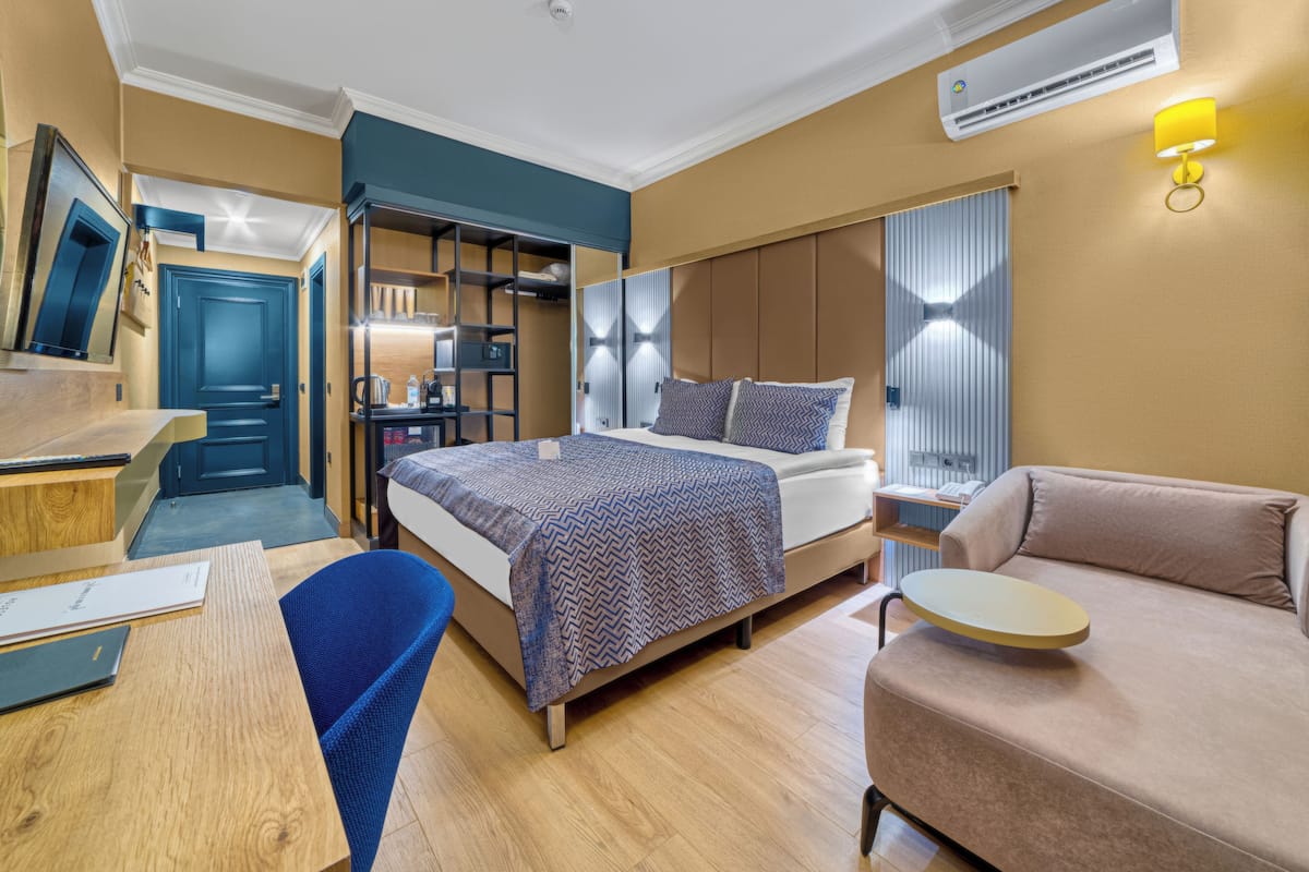 A modern hotel room with a bed, a sofa, a desk, and a wardrobe.