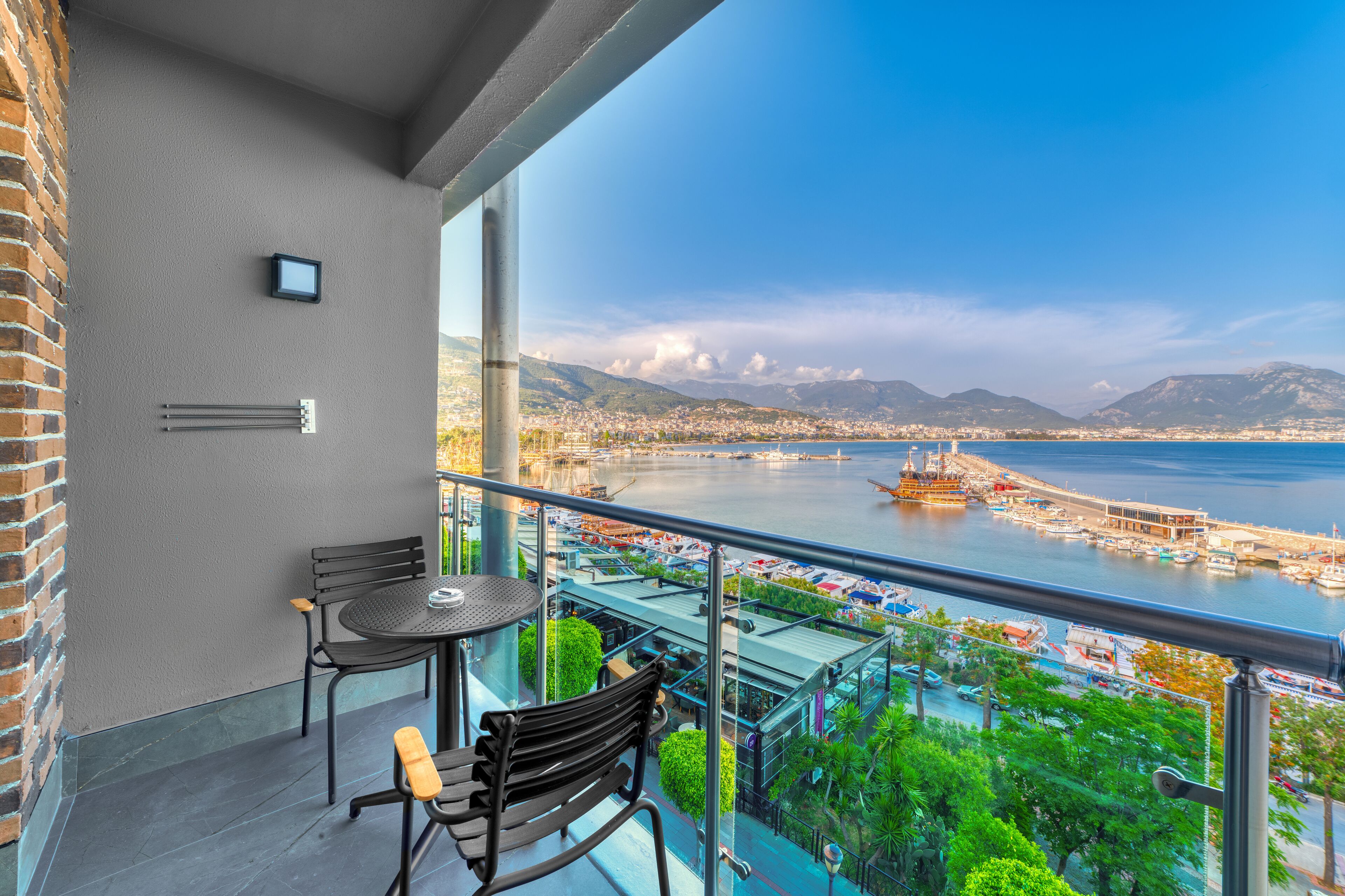 A balcony with a table and chairs, overlooking a marina with boats and a cityscape.