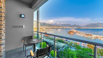 A balcony with a table and chairs, overlooking a marina with boats and a cityscape.