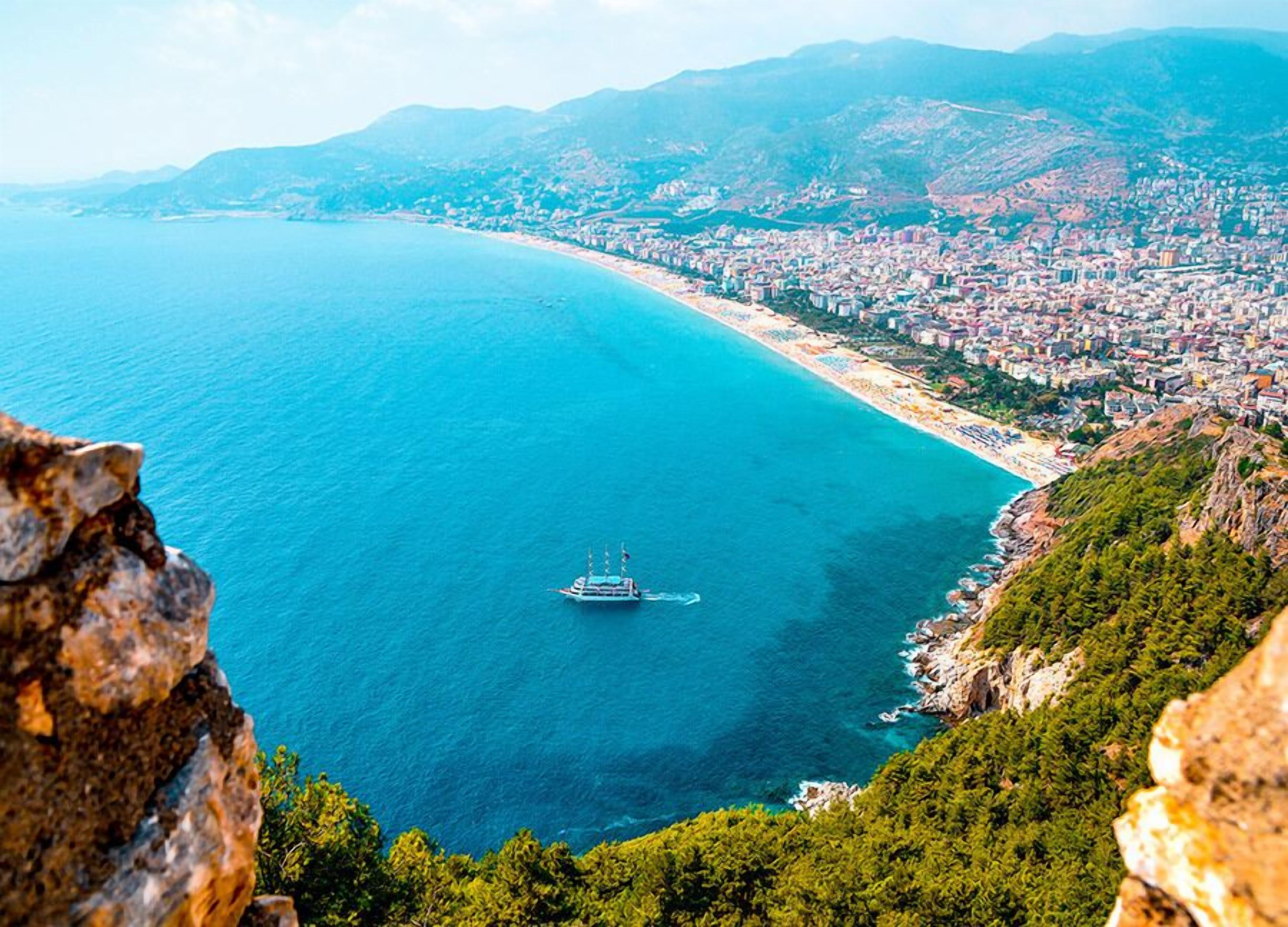 A coastal city with a beach, a boat, and mountainous terrain.