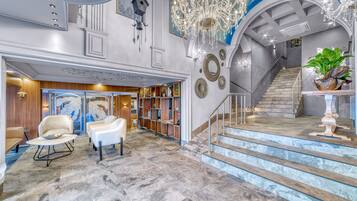 A spacious lobby with marble flooring, a grand staircase, and a chandelier.