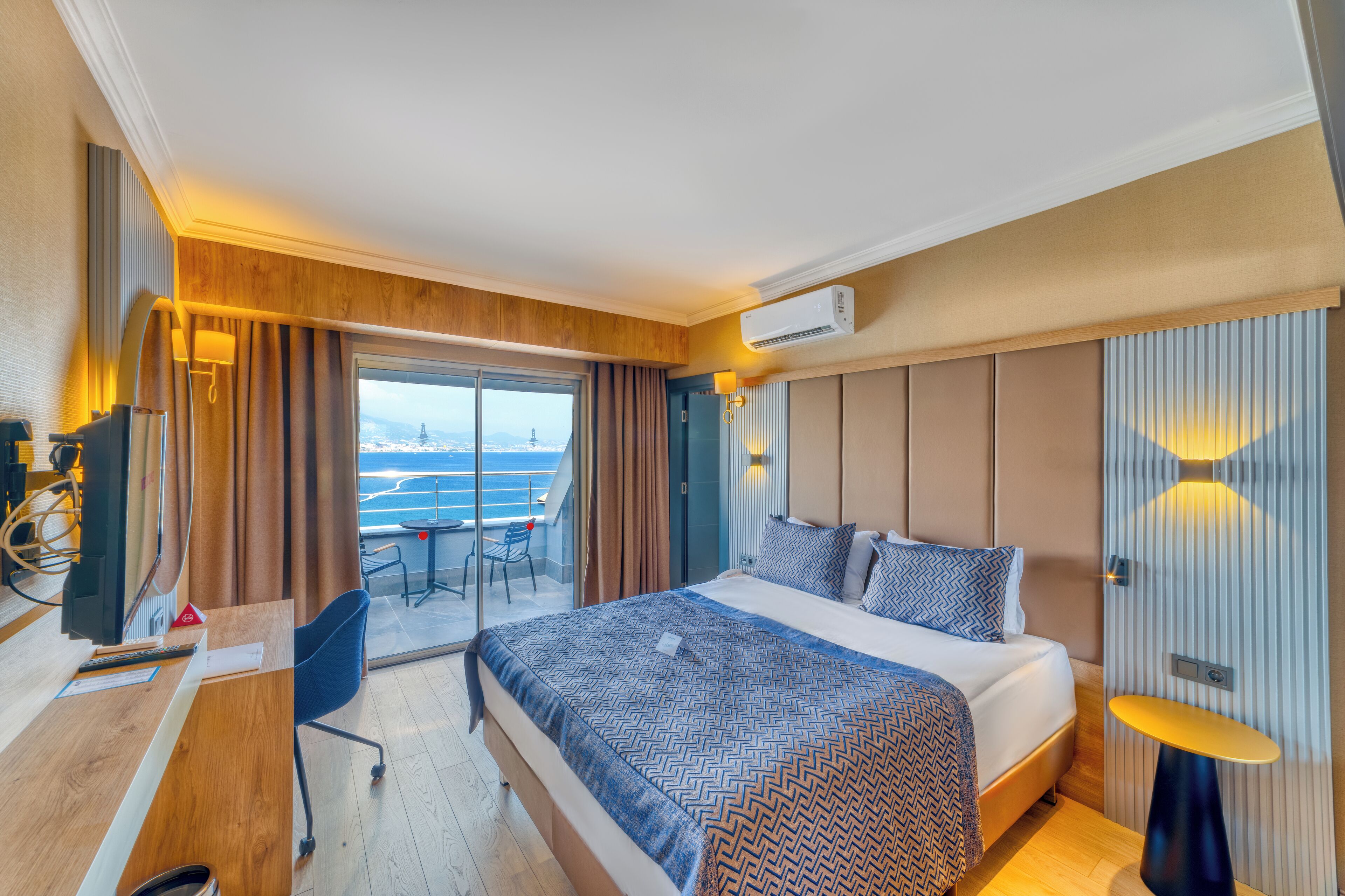 Habitación de hotel con una cama grande, un escritorio con computadora, una silla y vista al mar.