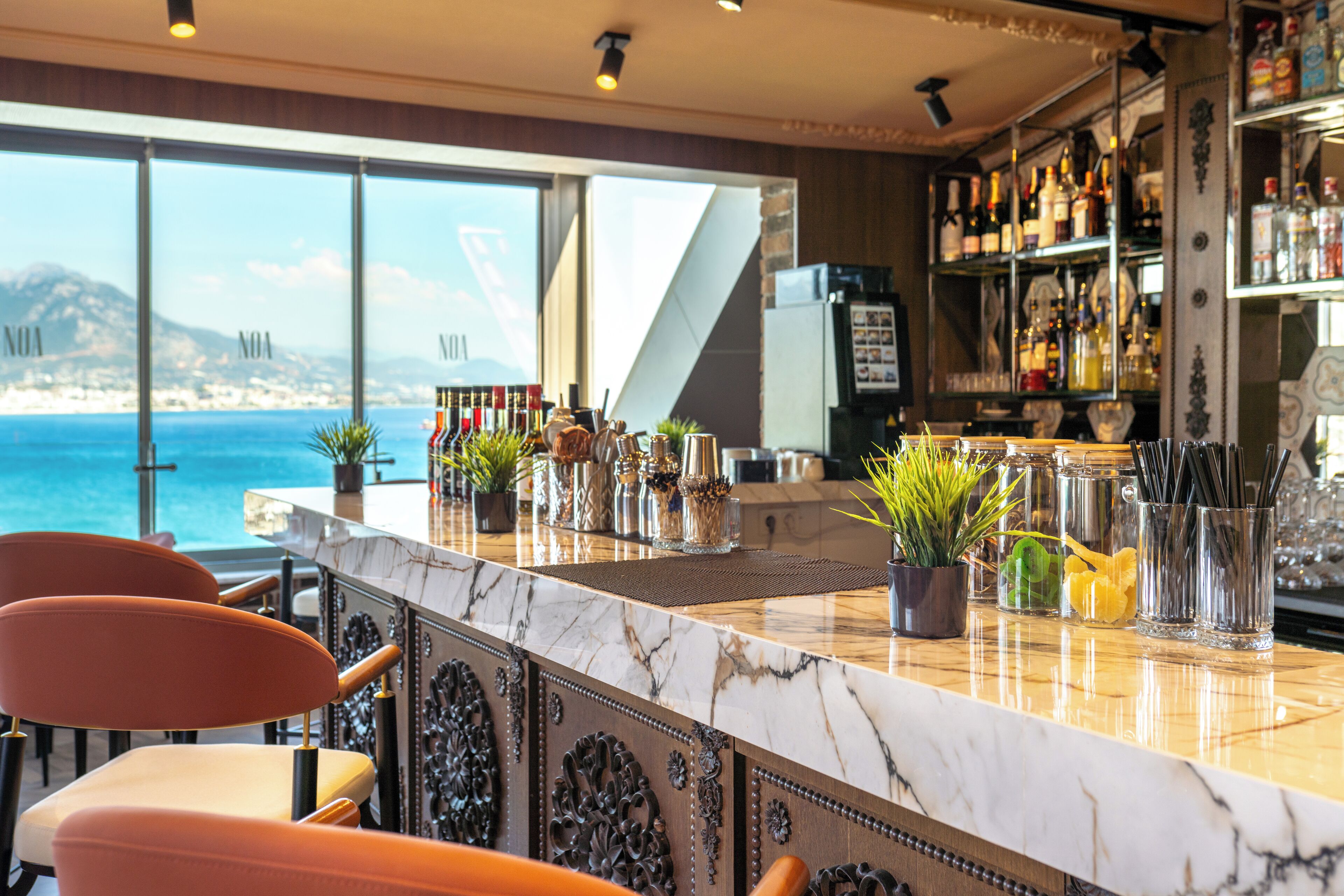 Un espace bar doté d’un comptoir en marbre, de plantes en pot et offrant une vue sur la mer.
